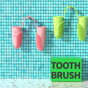 Pink and green silicone toothbrushes on a blue tiled background with a sign below them.